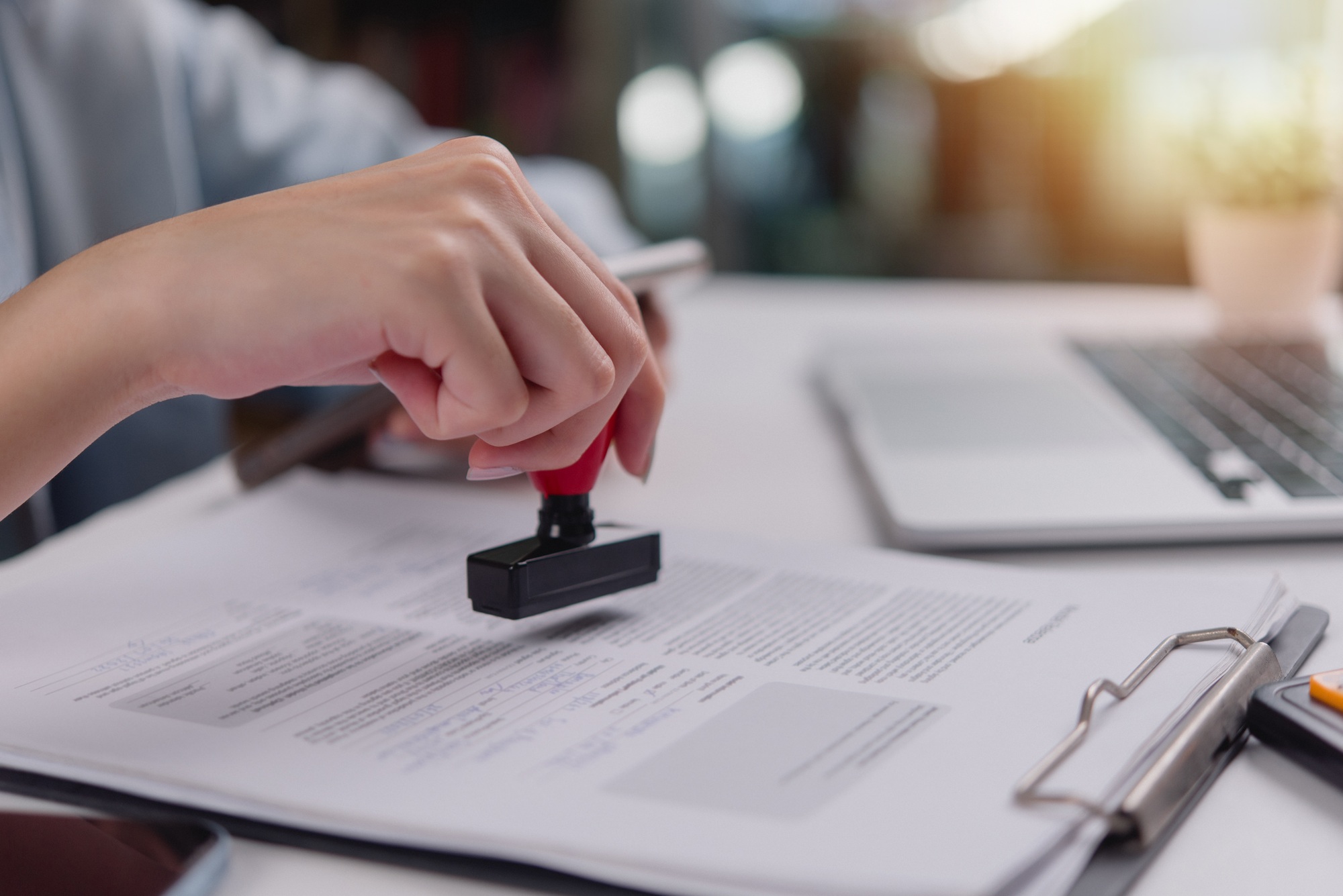 hand using a red stamp on a legal document, confirmation or validation in administrative work.